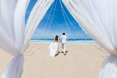 Newlyweds holding hands hugging at white sandy tropical caribbea